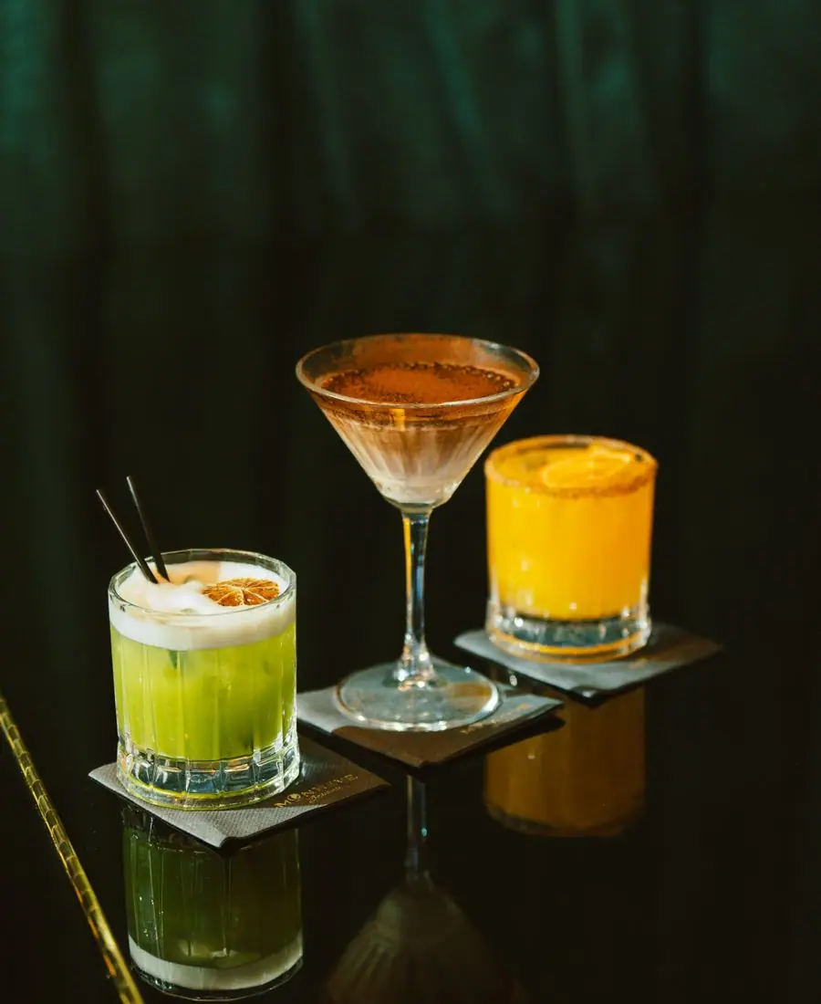 Vibrant non-alcoholic cocktail with fresh berries and mint in a coupe, glowing jewel-toned under bar light