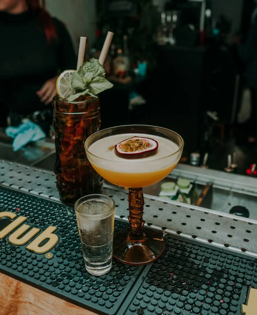Glass of amber whiskey served neat catching golden light beside a bottle on a dark wooden bar